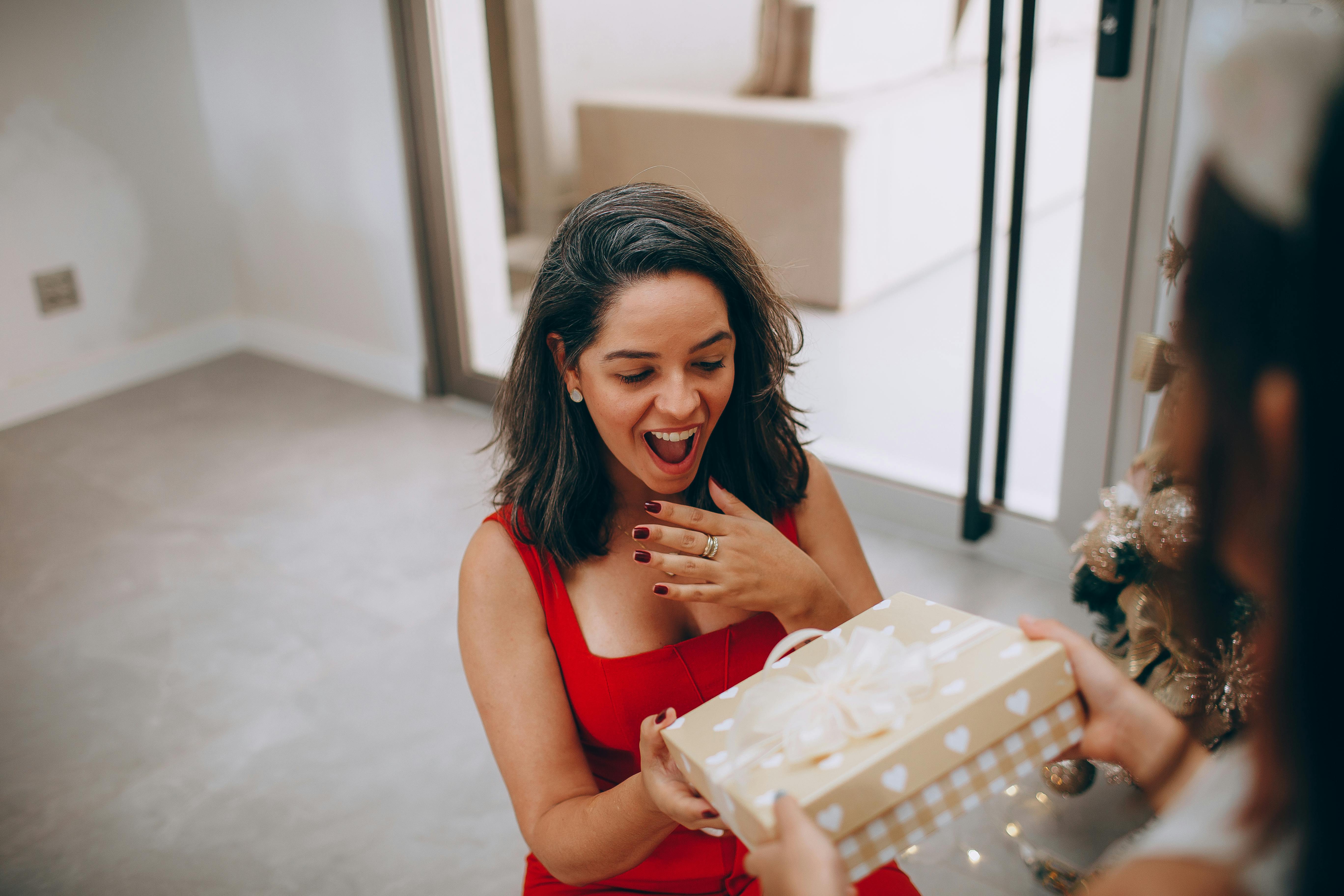 Free Woman in red dress excited to receive a Christmas gift indoors. Stock Photo