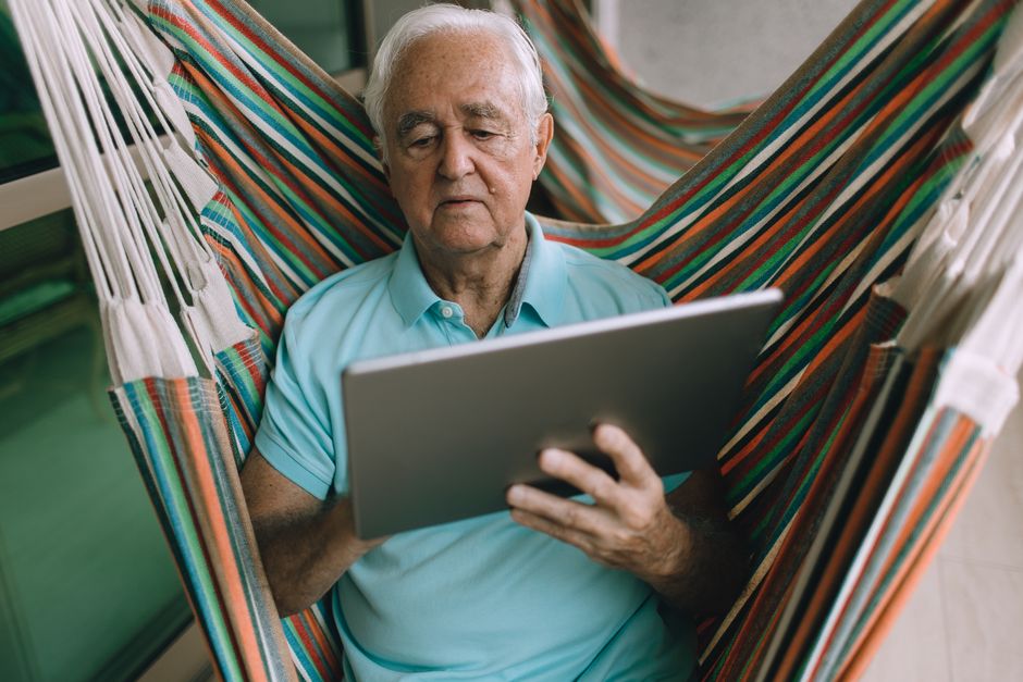 Elderly man relaxing in a hammock while using a tablet, embracing modern technology.