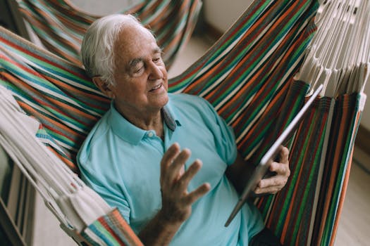 Elderly man enjoying leisure time in a hammock while using a tablet device.