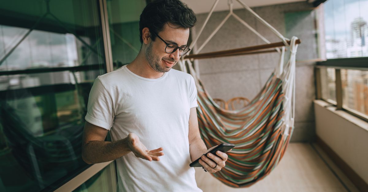 Homem adulto usando smartphone na varanda com uma rede, transmitindo um estilo de vida relaxado.