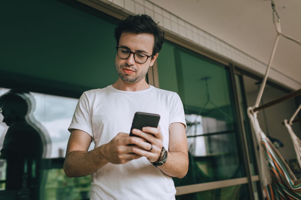 A young man texting on his smartphone outdoors on a balcony