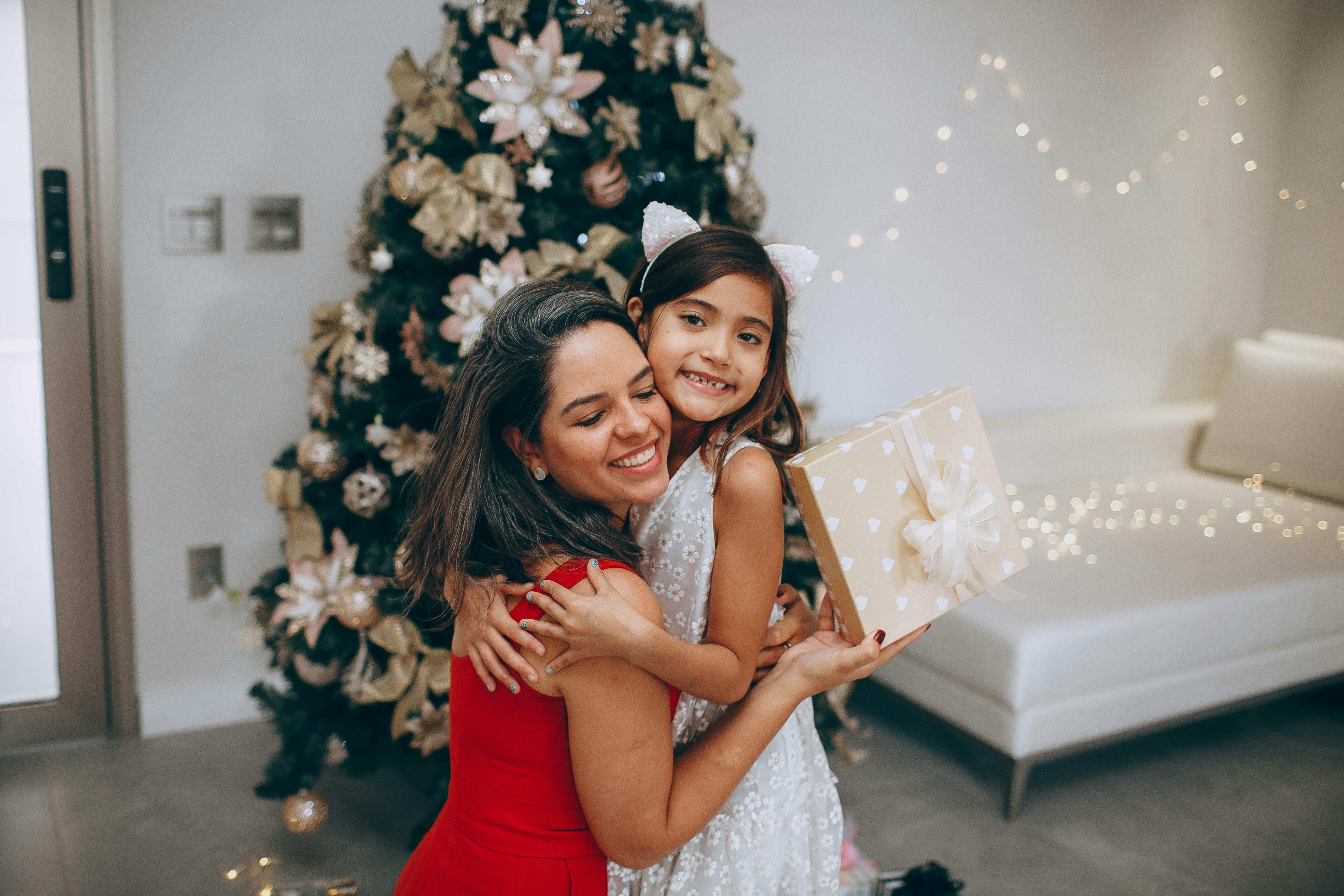 mother and daughter hugging with christmas tree behind