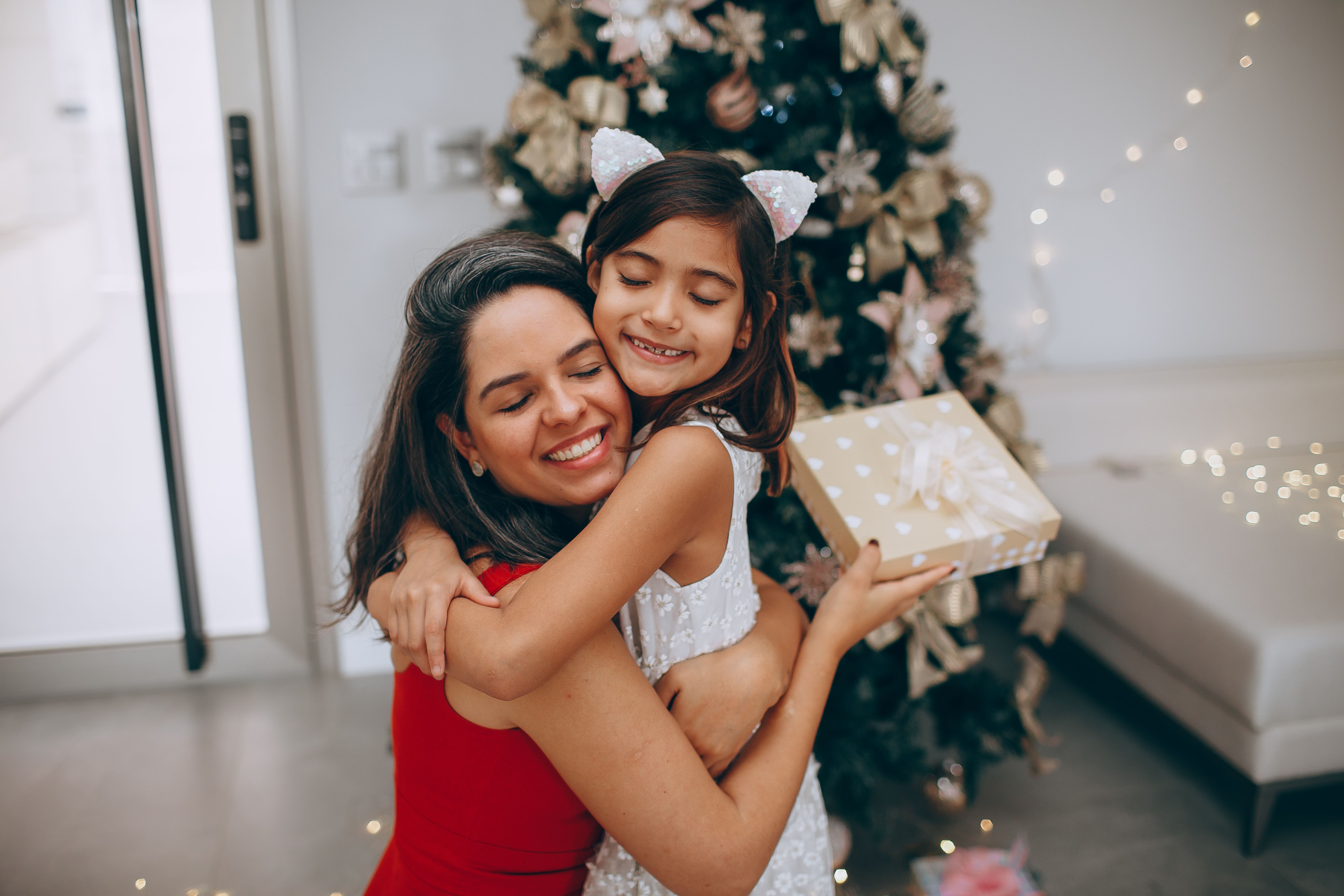 A Woman and a Girl in a Hug Against a Christmas Tree · Free Stock Photo