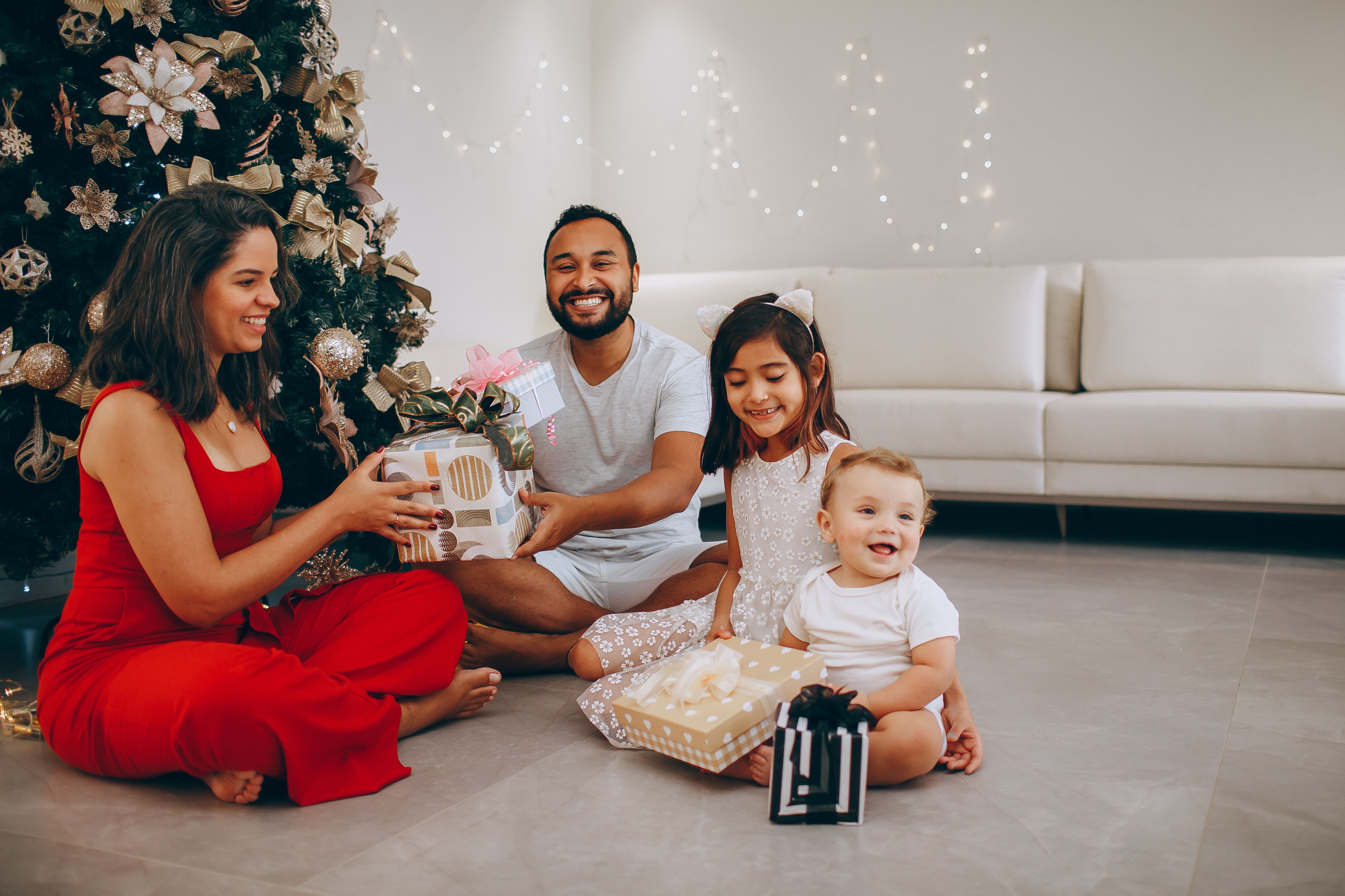 Family gathered around a Christmas tree, exchanging gifts with joyful smiles indoors.