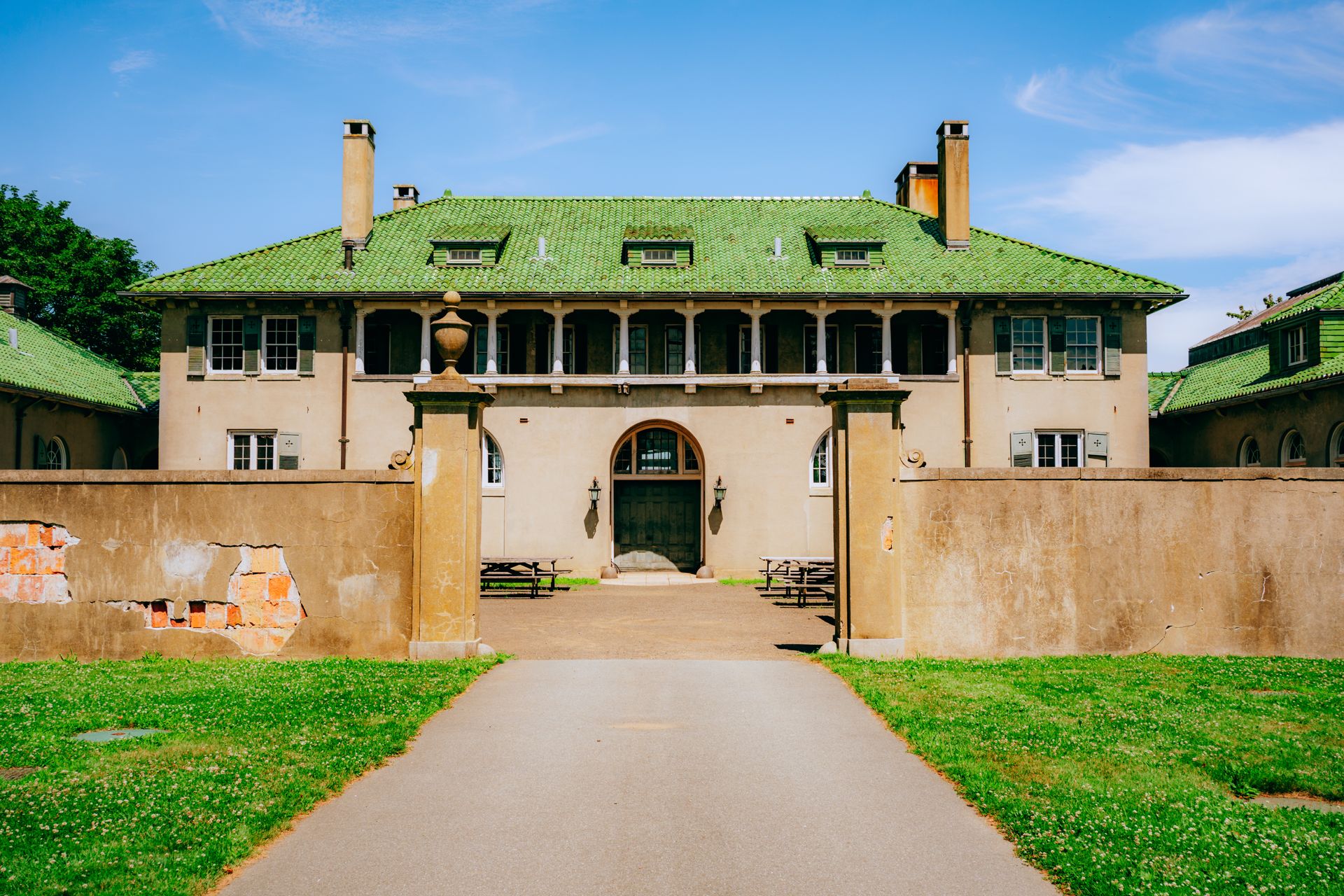 A classic mansion with a green roof and courtyard in a sunny park setting, perfect for travel enthusiasts.