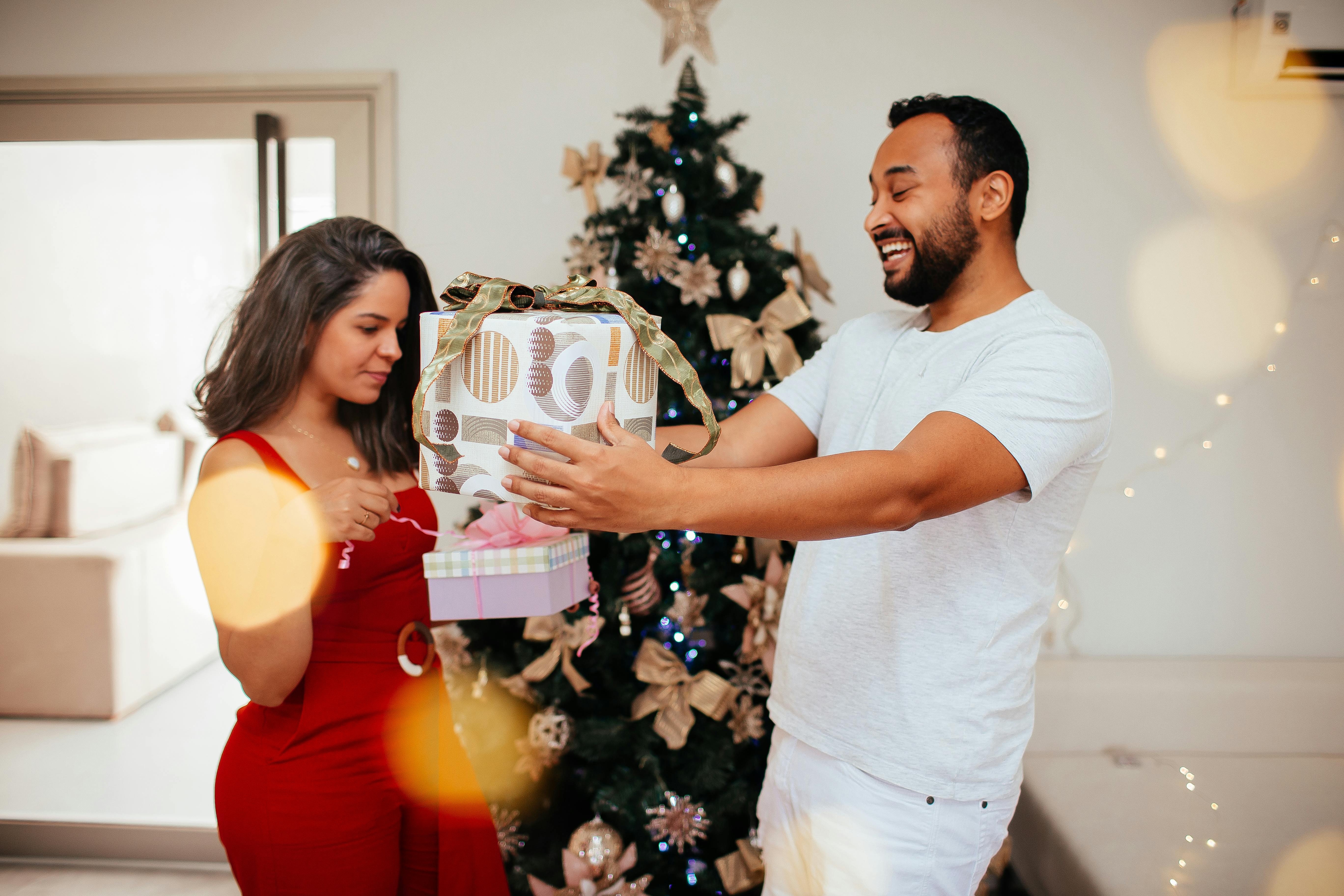 Joyful couple exchanging gifts in front of a Christmas tree. Holiday spirit captured indoors.
