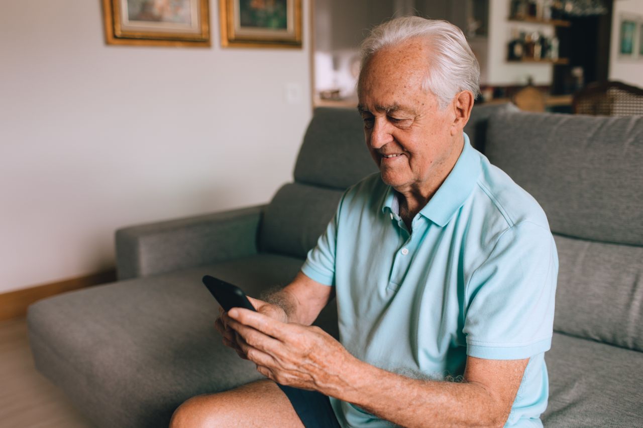 elderly man in a polo shirt using a smartphone indoors while sitting o