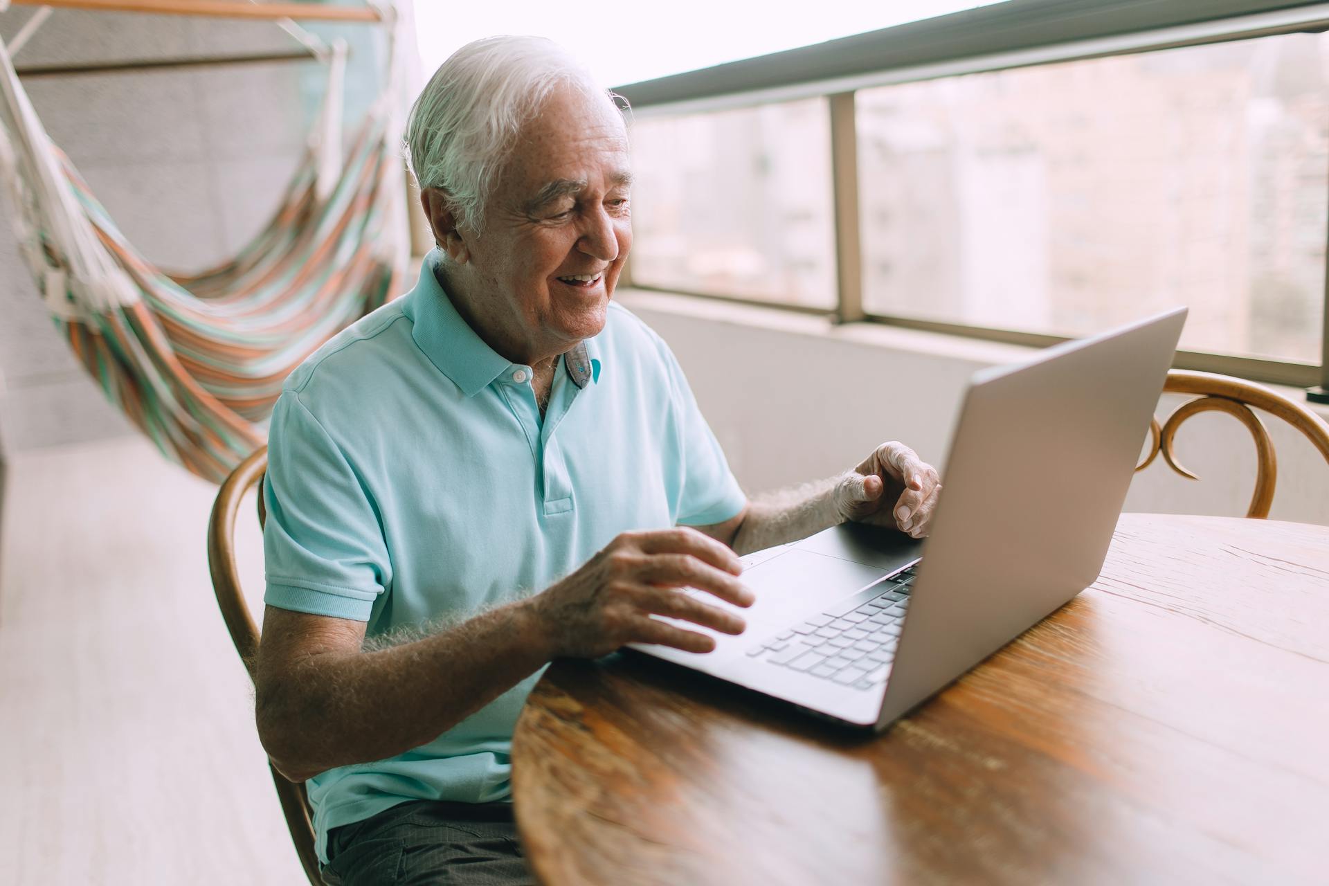 Senior man enjoying technology, using laptop comfortably on home balcony.