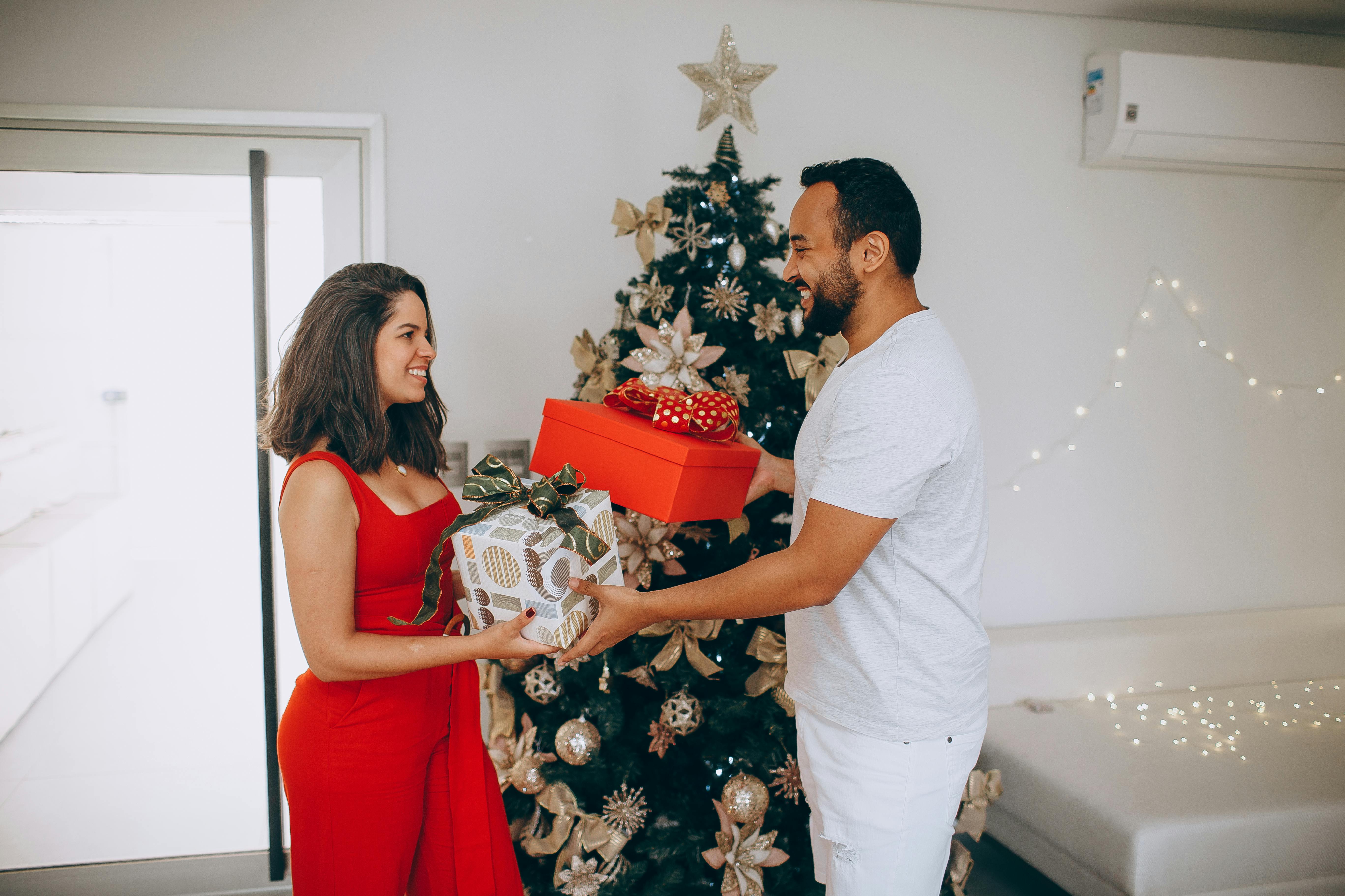 Joyful couple exchanging Christmas gifts by a festive tree indoors, celebrating the holiday season.