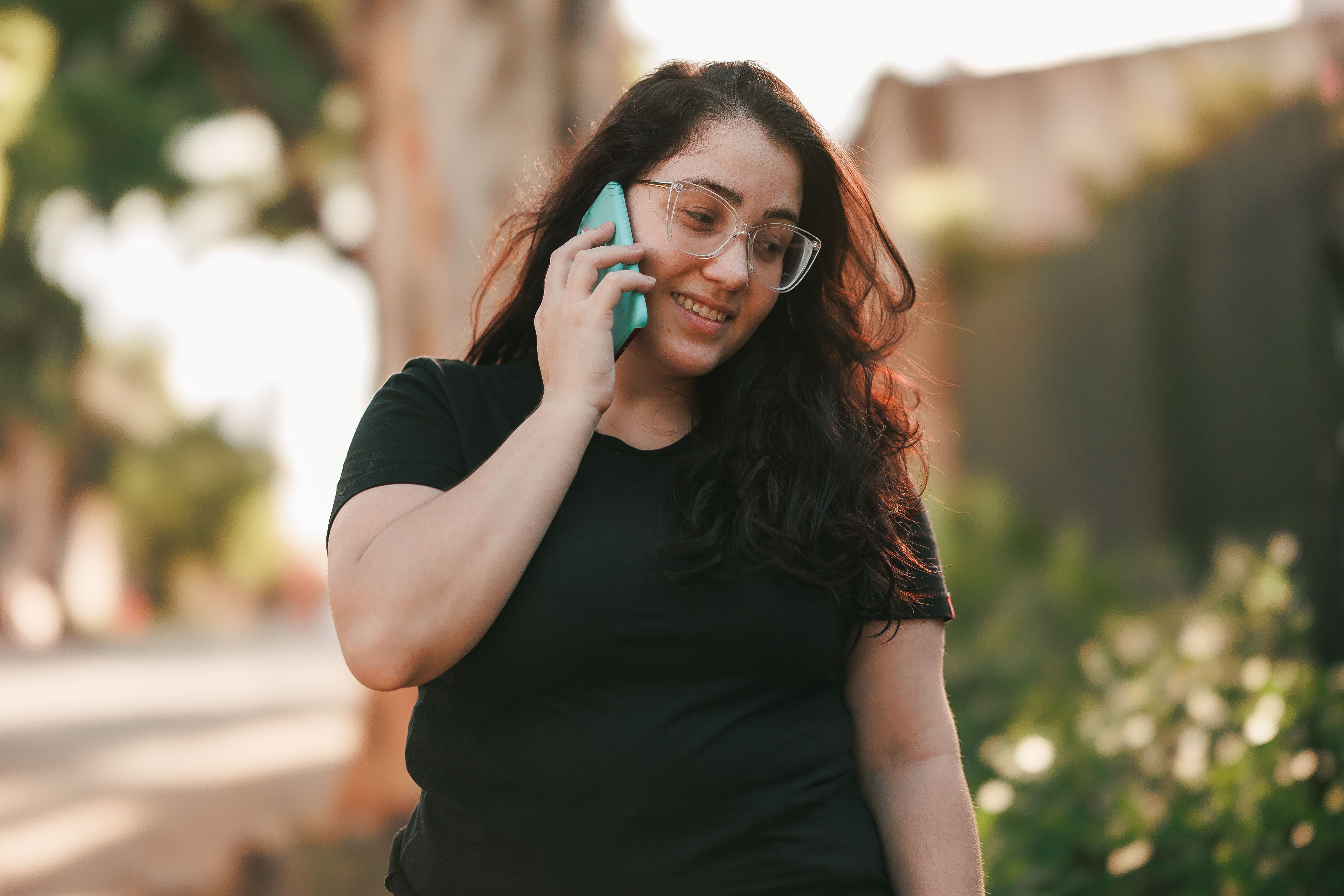 A woman with glasses talking into her smartphone outdoors on a warm day