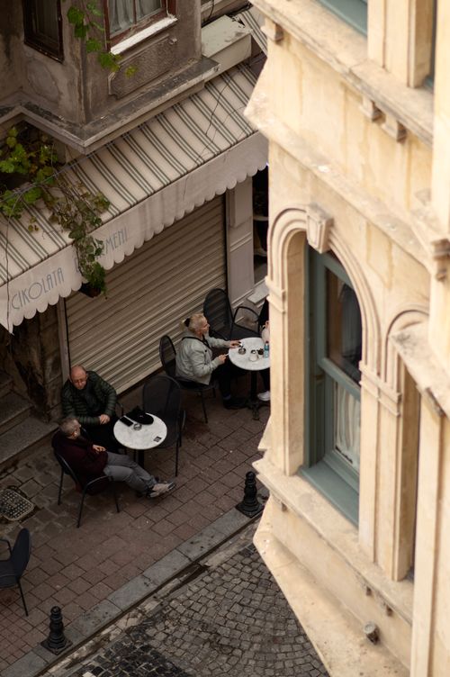 Free Aerial view of people relaxing outside a European café on a charming narrow street. Stock Photo