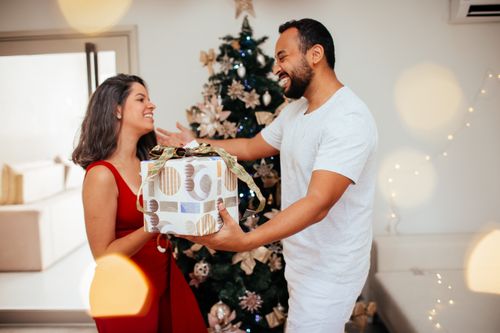 Free A happy couple exchanges Christmas gifts by a decorated tree indoors, full of festive cheer. Stock Photo