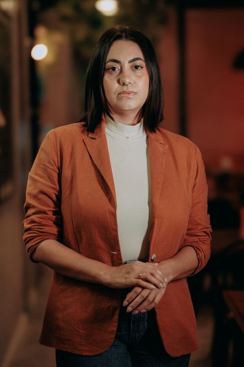 Free Professional portrait of a woman in an orange blazer indoors with dim lighting and neutral expression. Stock Photo