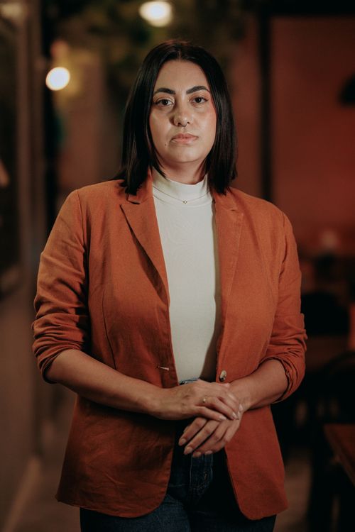Free Confident woman in orange blazer standing indoors with soft lighting. Stock Photo