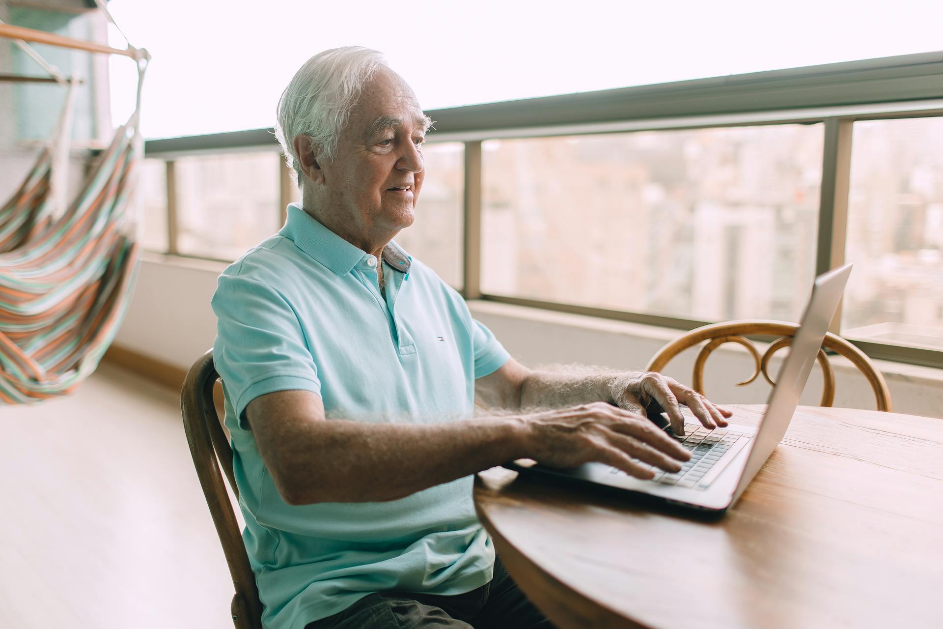 Elderly man enjoys his laptop on a balcony, symbolizing modern technology and active retirement lifestyle.