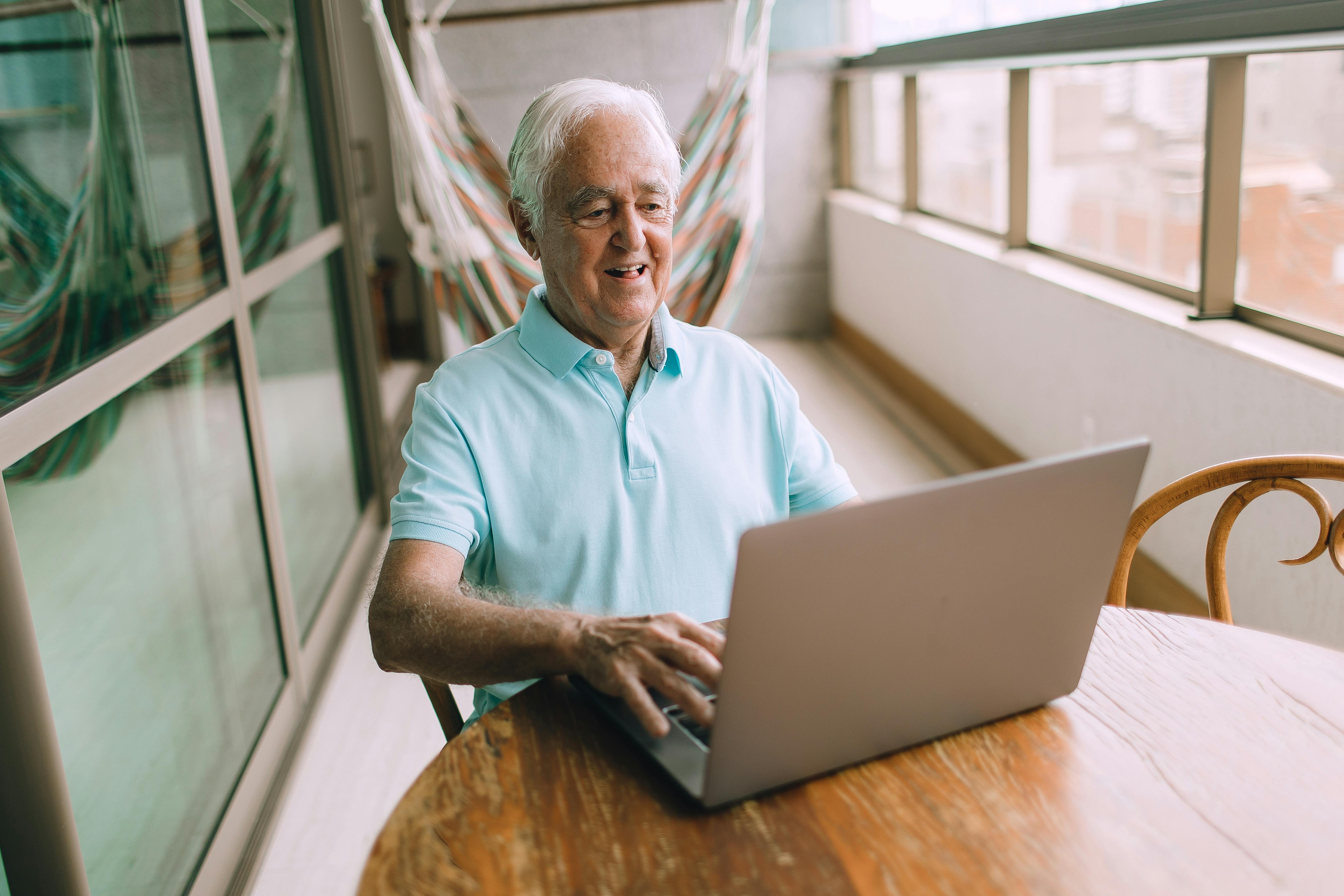 smiling senior man sitting at table with laptop on balcony