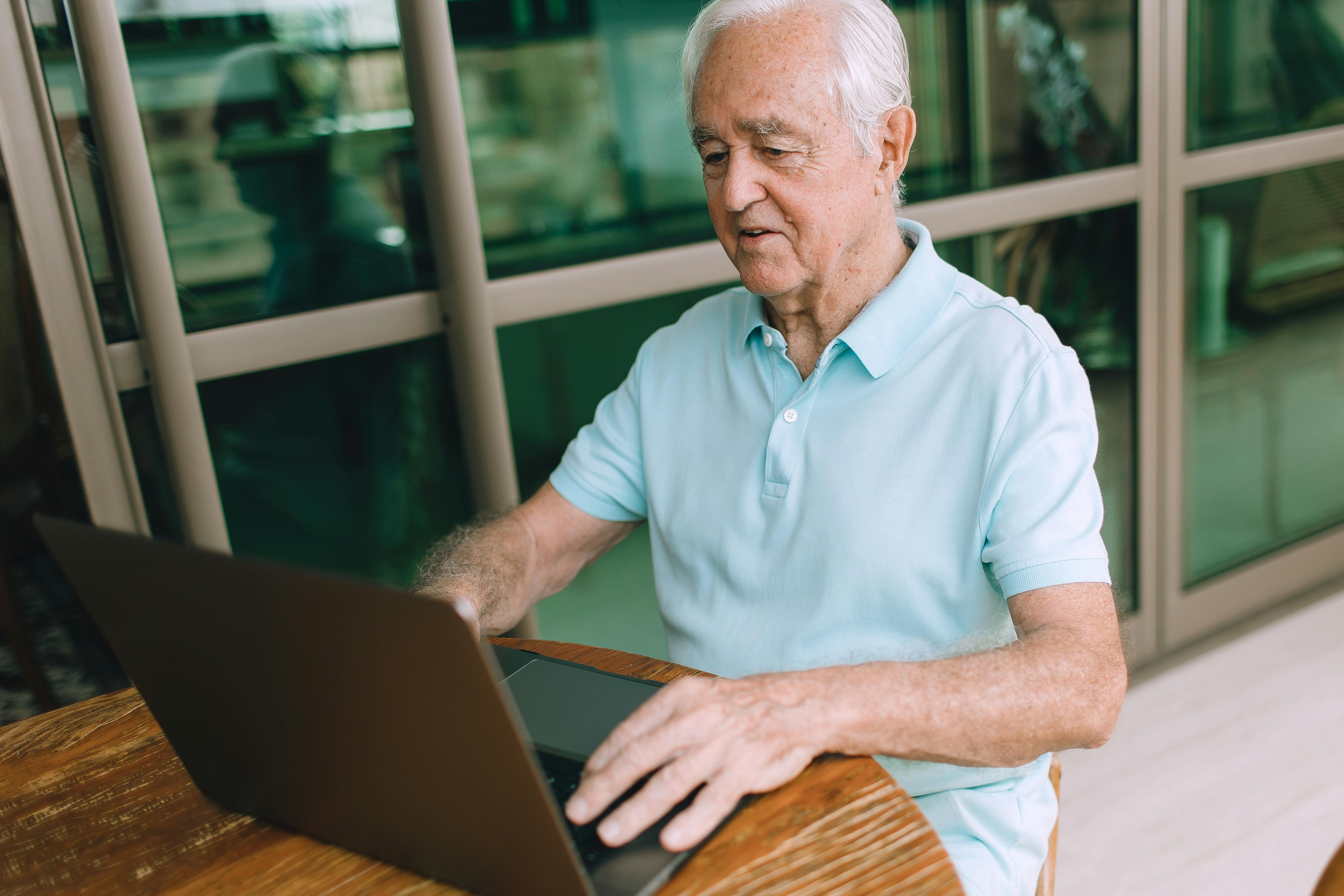 Elderly man enjoying technology, typing on laptop indoors.
