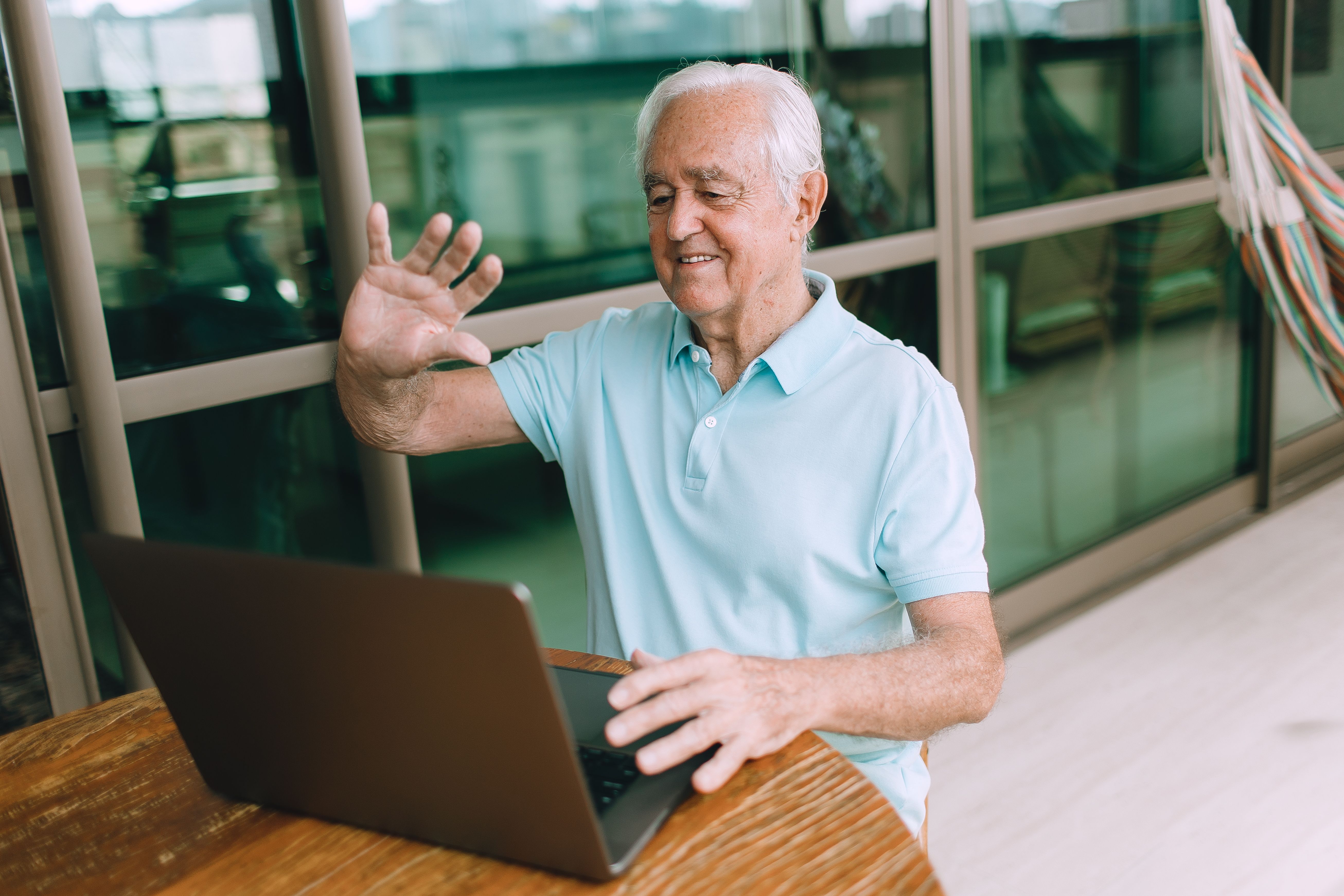Elderly man waving at laptop screen during a video call at home.