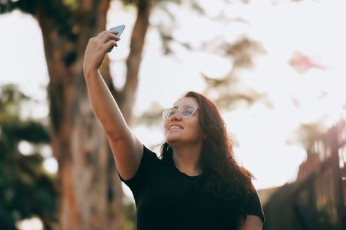 Free Smiling woman takes a selfie outdoors in bright sunlight, enjoying the day. Stock Photo