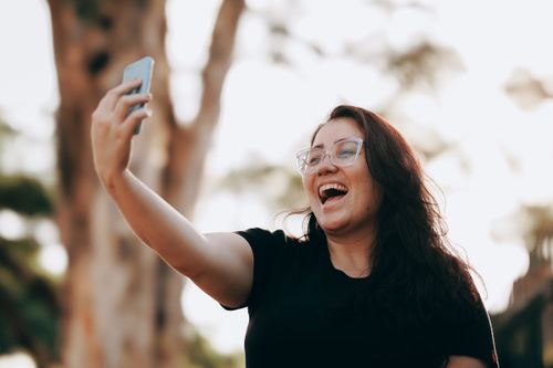 Free Smiling woman taking a selfie outdoors in a sunny park, capturing a joyful moment. Stock Photo