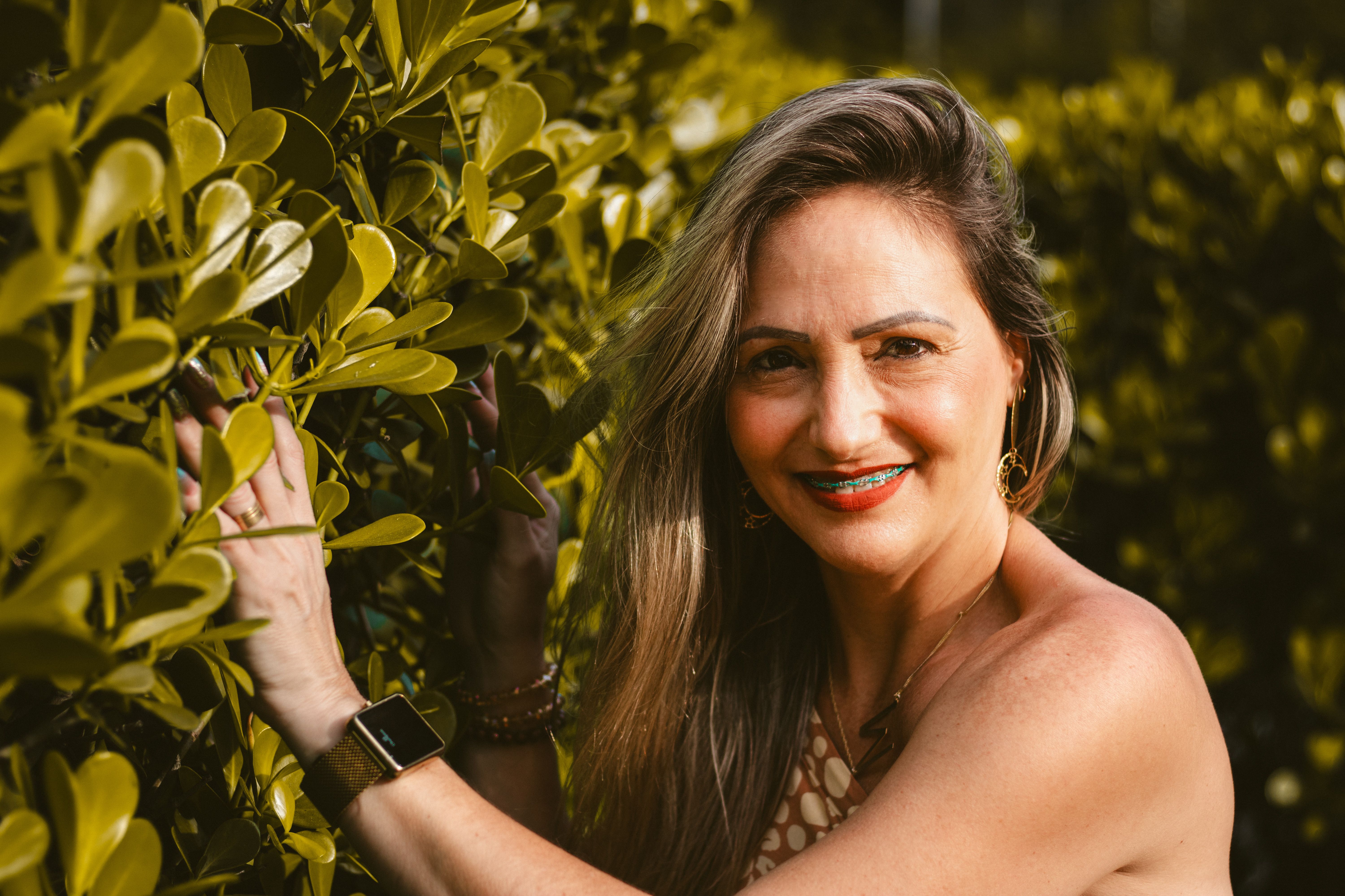 A cheerful woman with braces smiling amidst lush green foliage in a park setting.