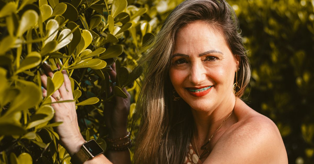 A cheerful woman with braces smiling amidst lush green foliage in a park setting.