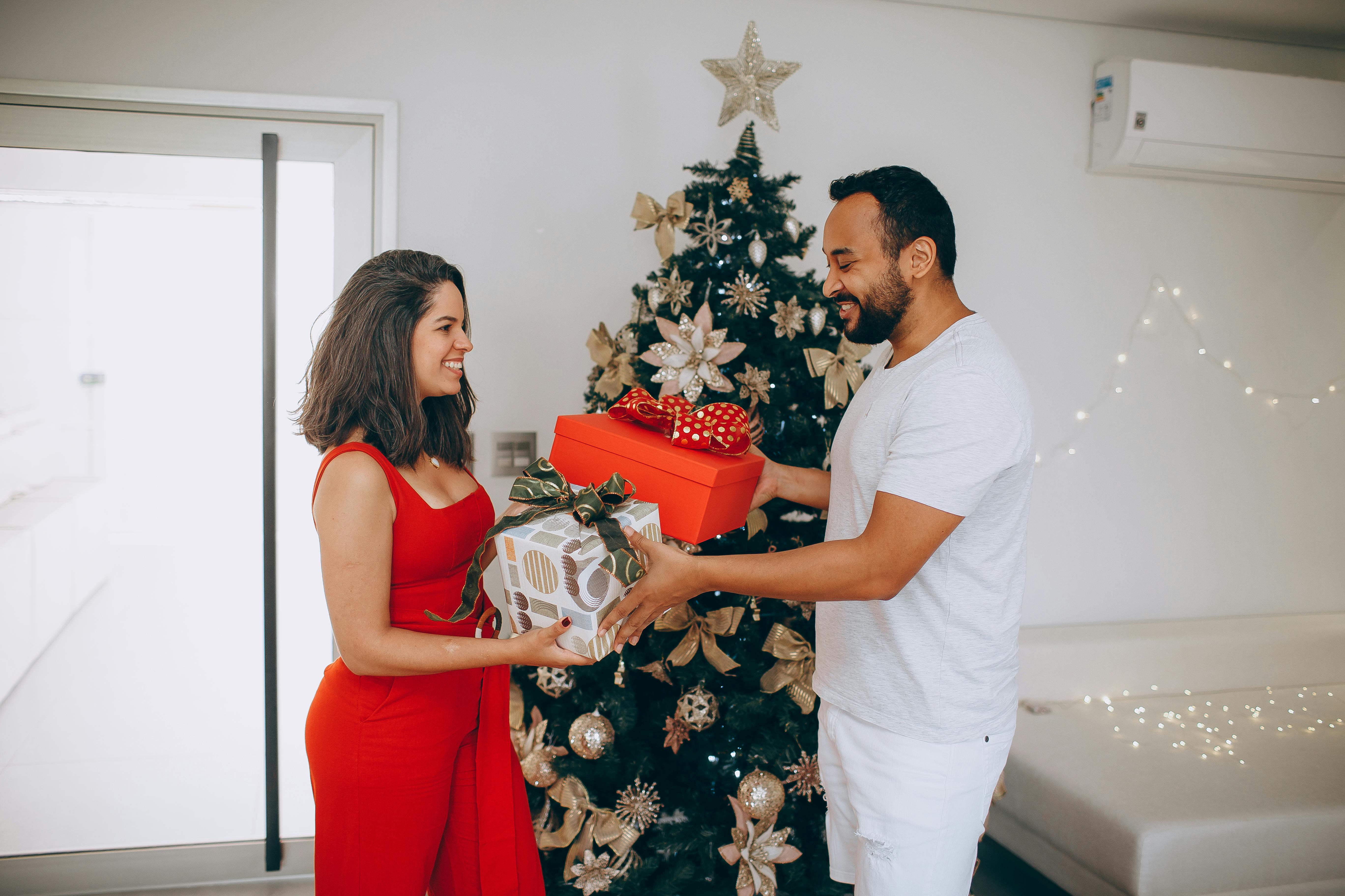 A joyful couple exchanging gifts in front of a beautifully decorated Christmas tree indoors.