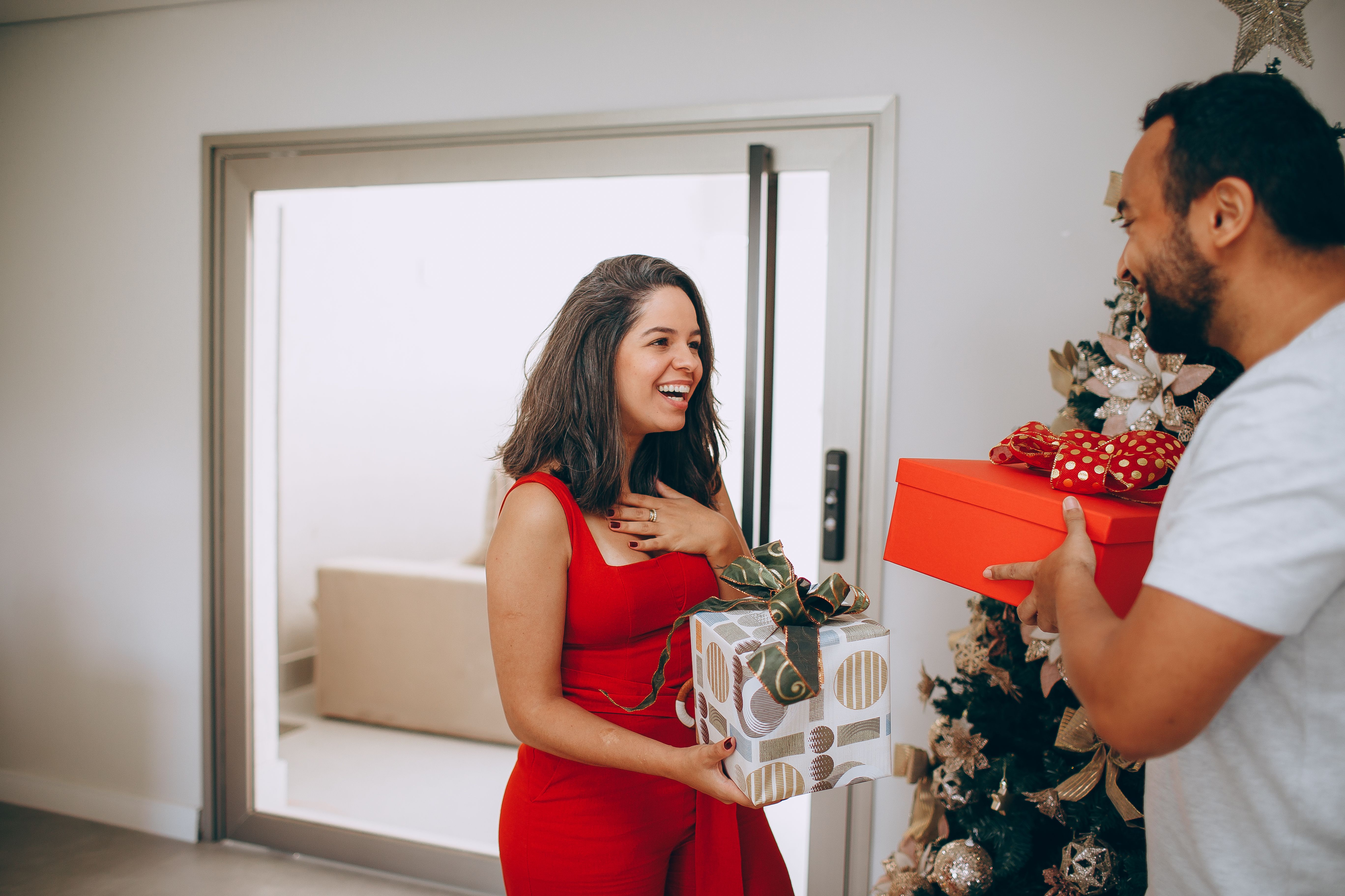 A couple exchanging gifts in a festive home setting with a Christmas tree.