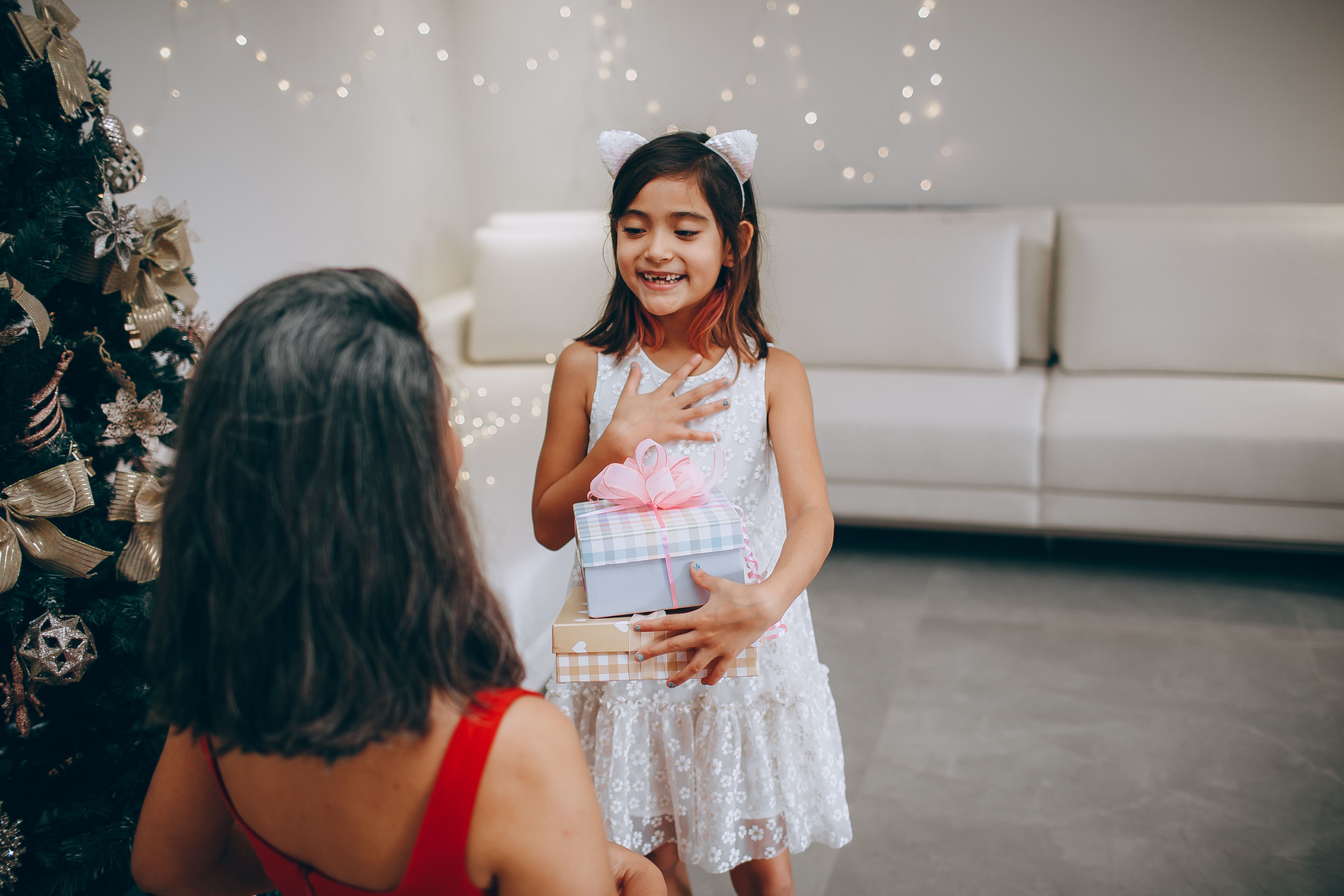 A joyful moment of a mother and daughter exchanging Christmas gifts indoors by the tree.