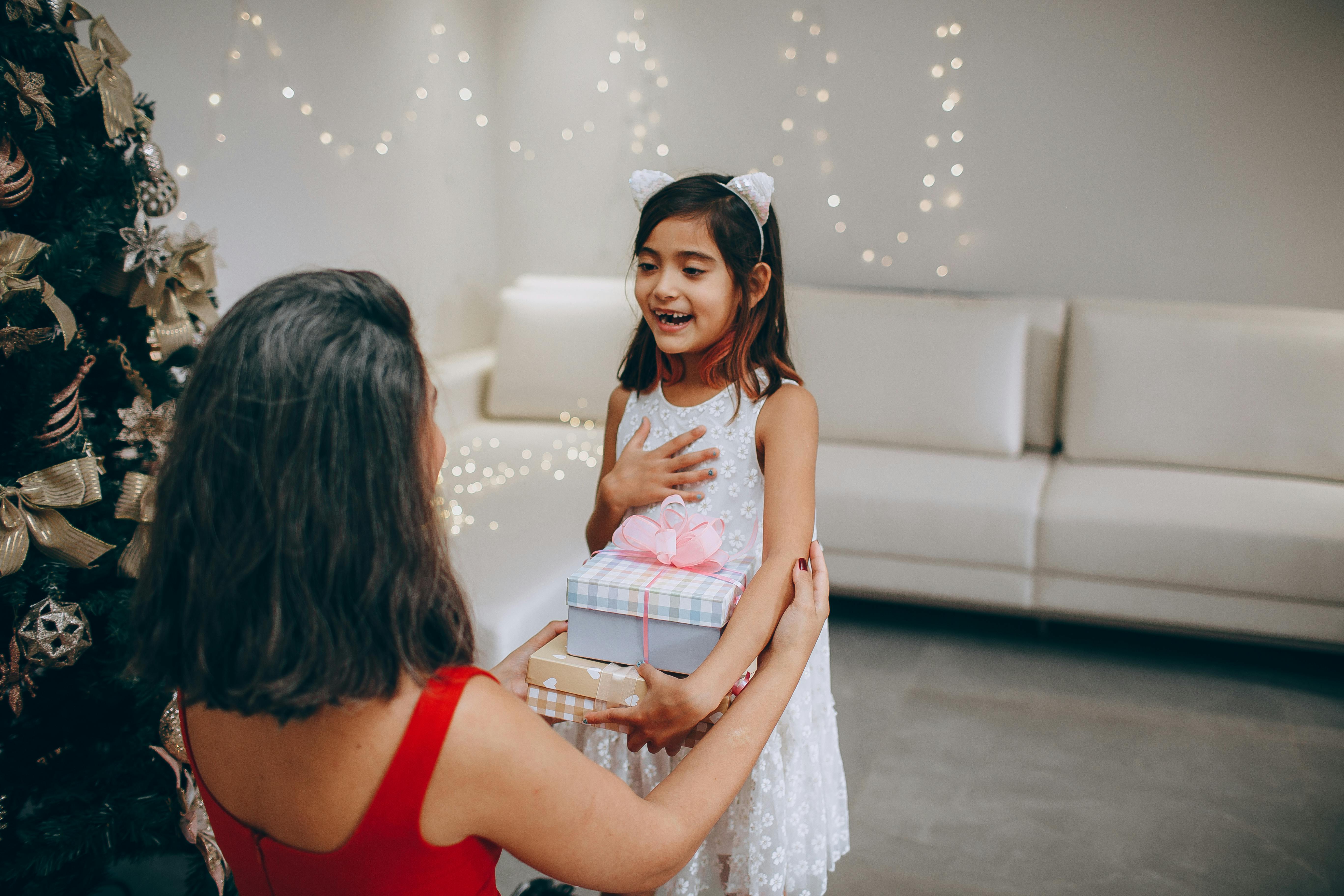 A joyful moment as a mother gives Christmas gifts to her delighted daughter indoors.