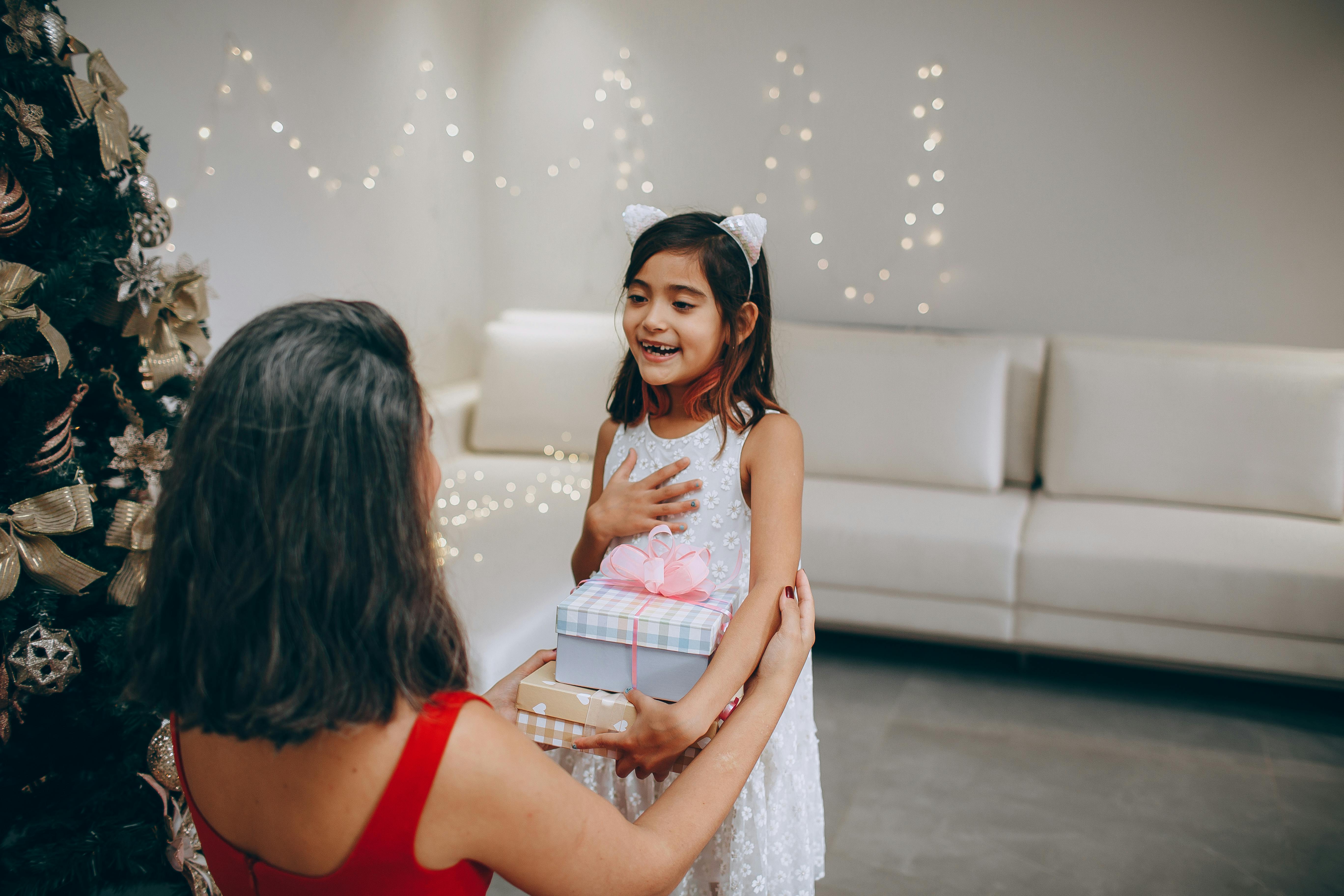A young girl joyfully receives a Christmas gift indoors, full of surprise and happiness.