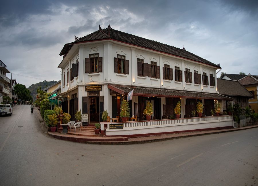 Elegant colonial-style building at a street corner in Luang Prabang, Laos, under cloudy skies.