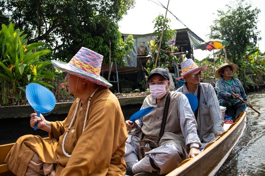 Group of adults on a traditional boat ride through a Southeast Asian canal, wearing colorful hats.