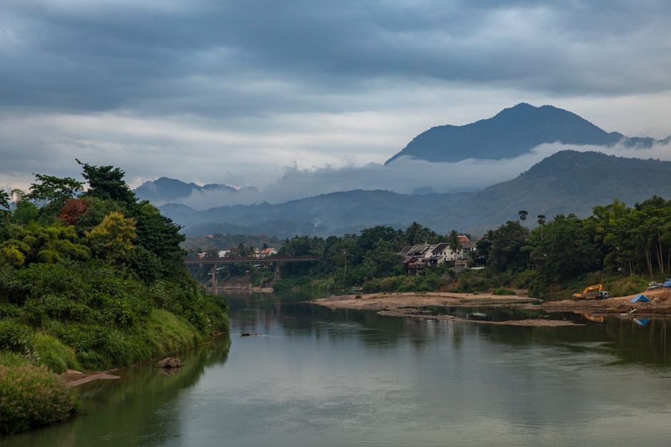 Serene view of a river and mountain landscape under cloudy skies in Laos.