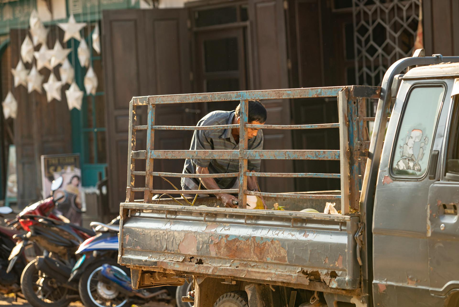 A man working on an old truck in a bustling urban area surrounded by motorbikes.