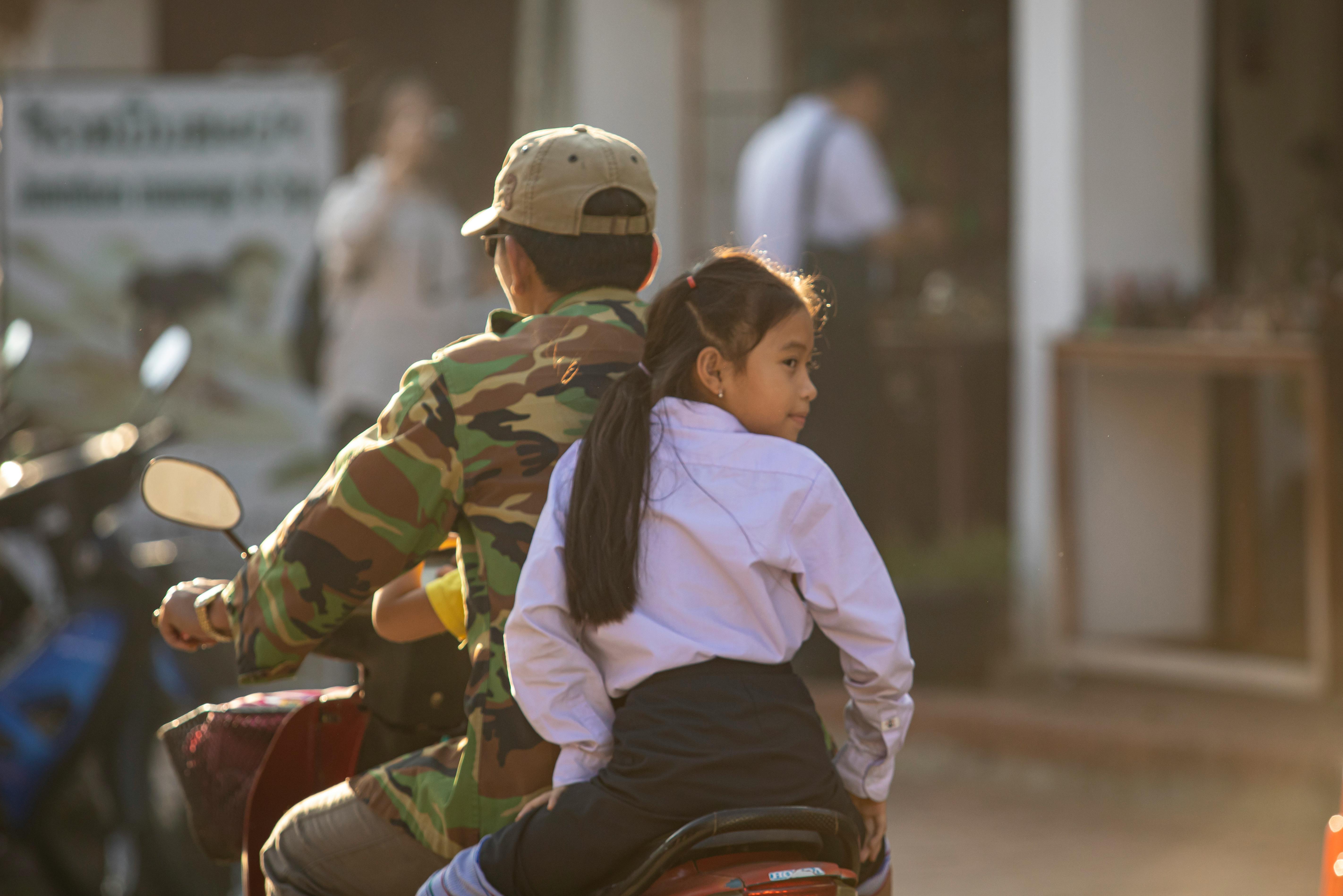 A father and daughter enjoying a motorbike ride together in a sunny outdoor setting.