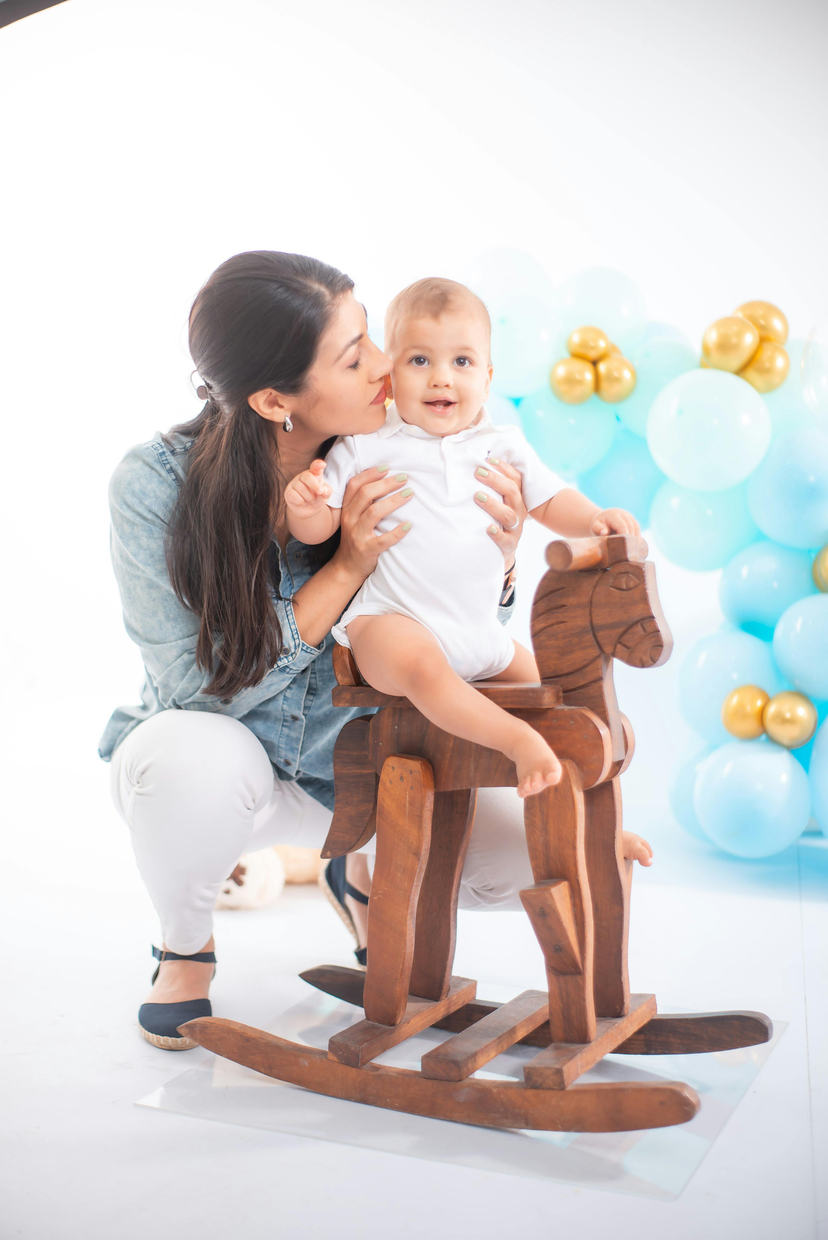 mother squatting and hugging baby on wooden horse