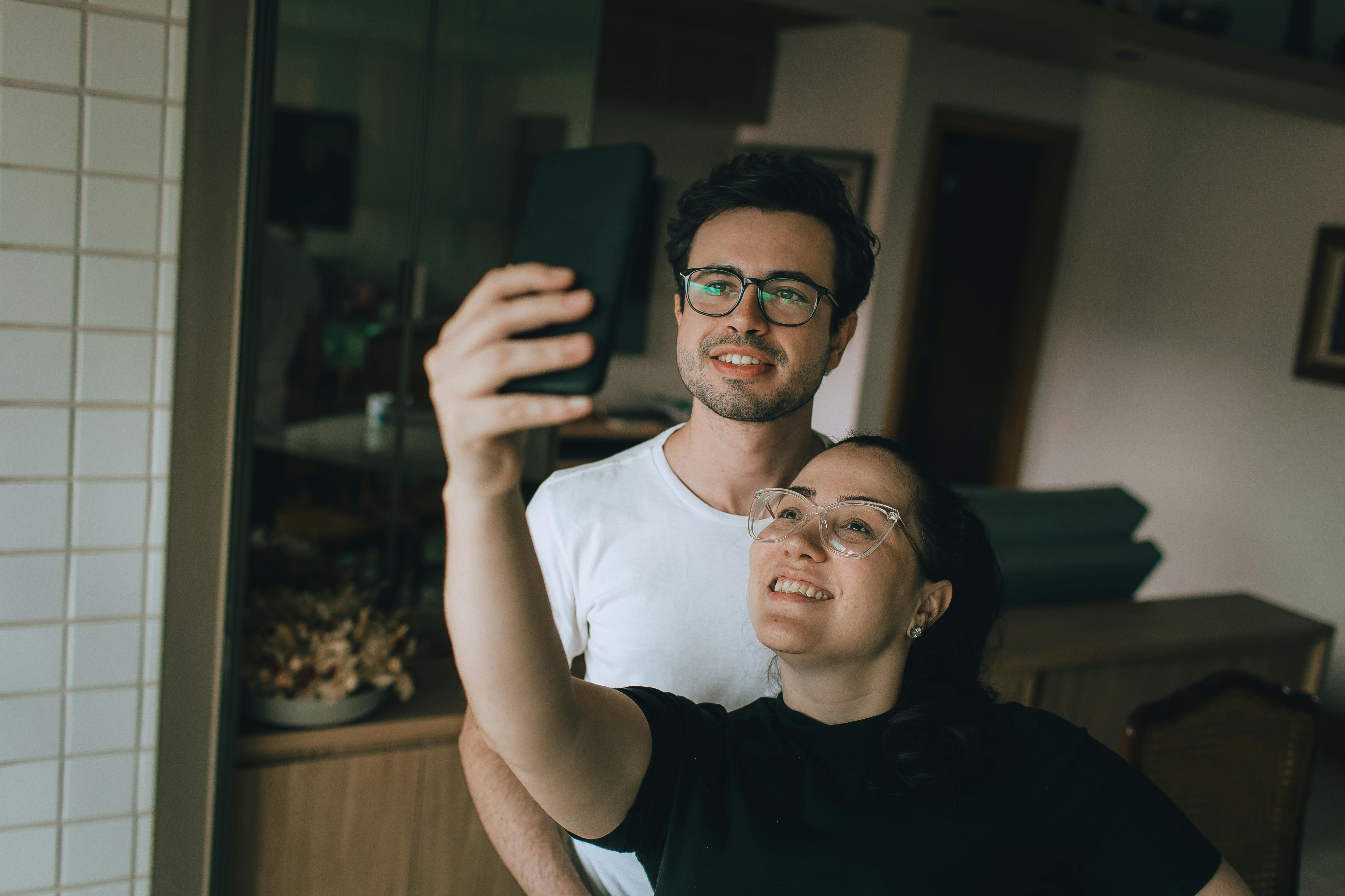 A couple happily taking a selfie indoors, reflecting a cozy and relaxed home atmosphere.