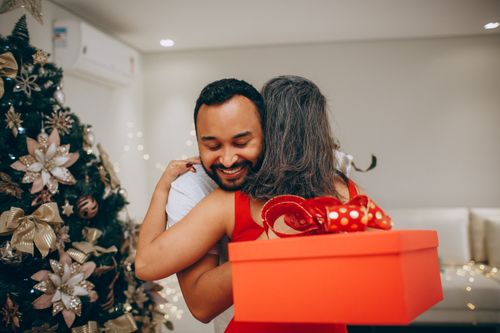 Free A joyful moment of hugging while exchanging gifts by a Christmas tree. Stock Photo