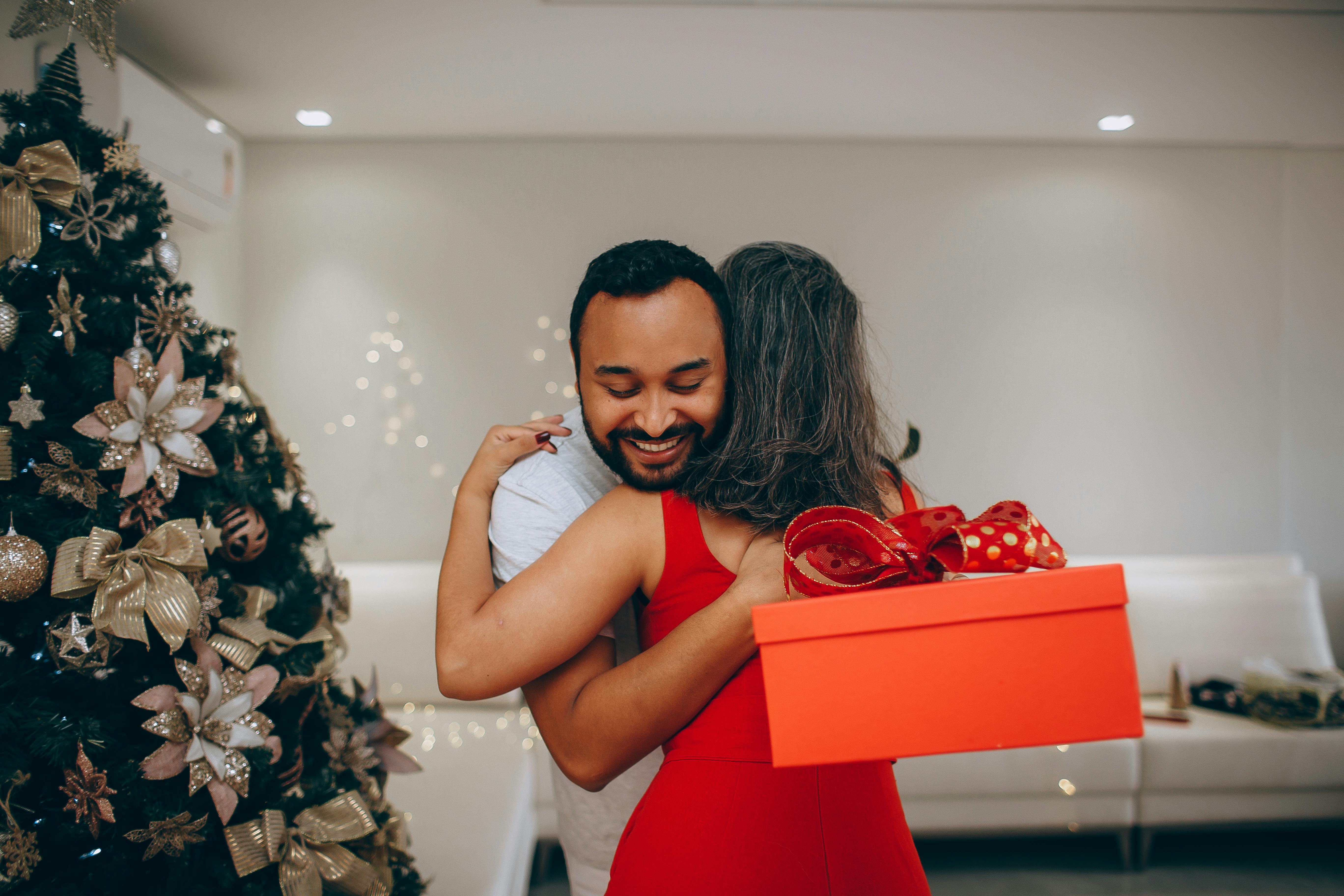 Happy couple hugging near a beautifully decorated Christmas tree with a gift box in hand.