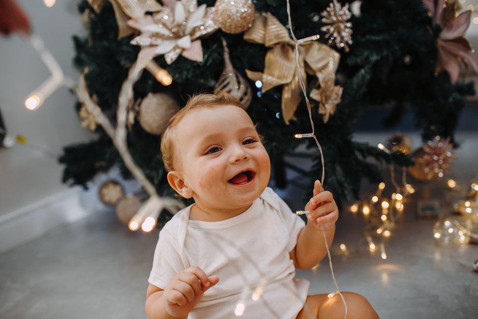 Adorable baby playing with Christmas lights by a decorated tree indoors.
