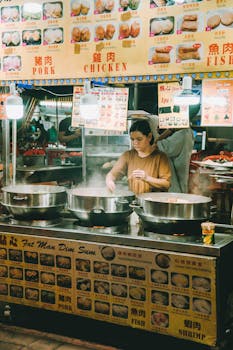An Asian woman cooking dim sum at a vibrant street food stall in Kuala Lumpur.