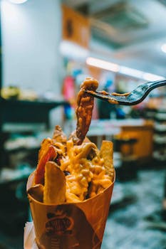 Close-up of cheesy fries with bacon in Kuala Lumpur's vibrant night market.