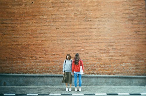 붉은 벽돌 벽 옆에 서있는 두 여자
