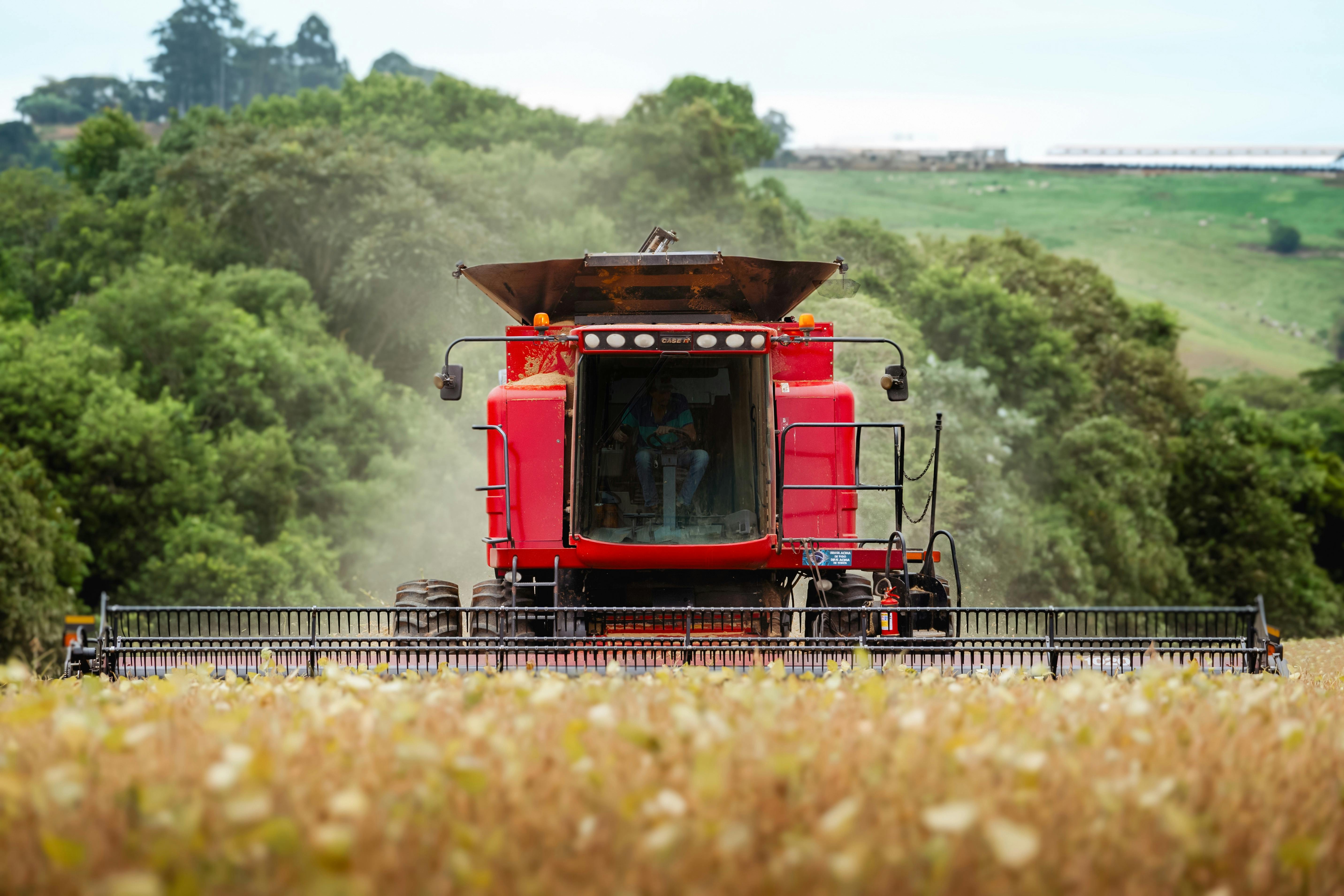 Free A red combine harvester in action during summer harvest in a lush green countryside. Stock Photo