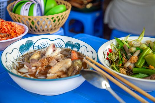 Delicious Asian noodle soup served with fresh vegetables and chopsticks on a blue table.