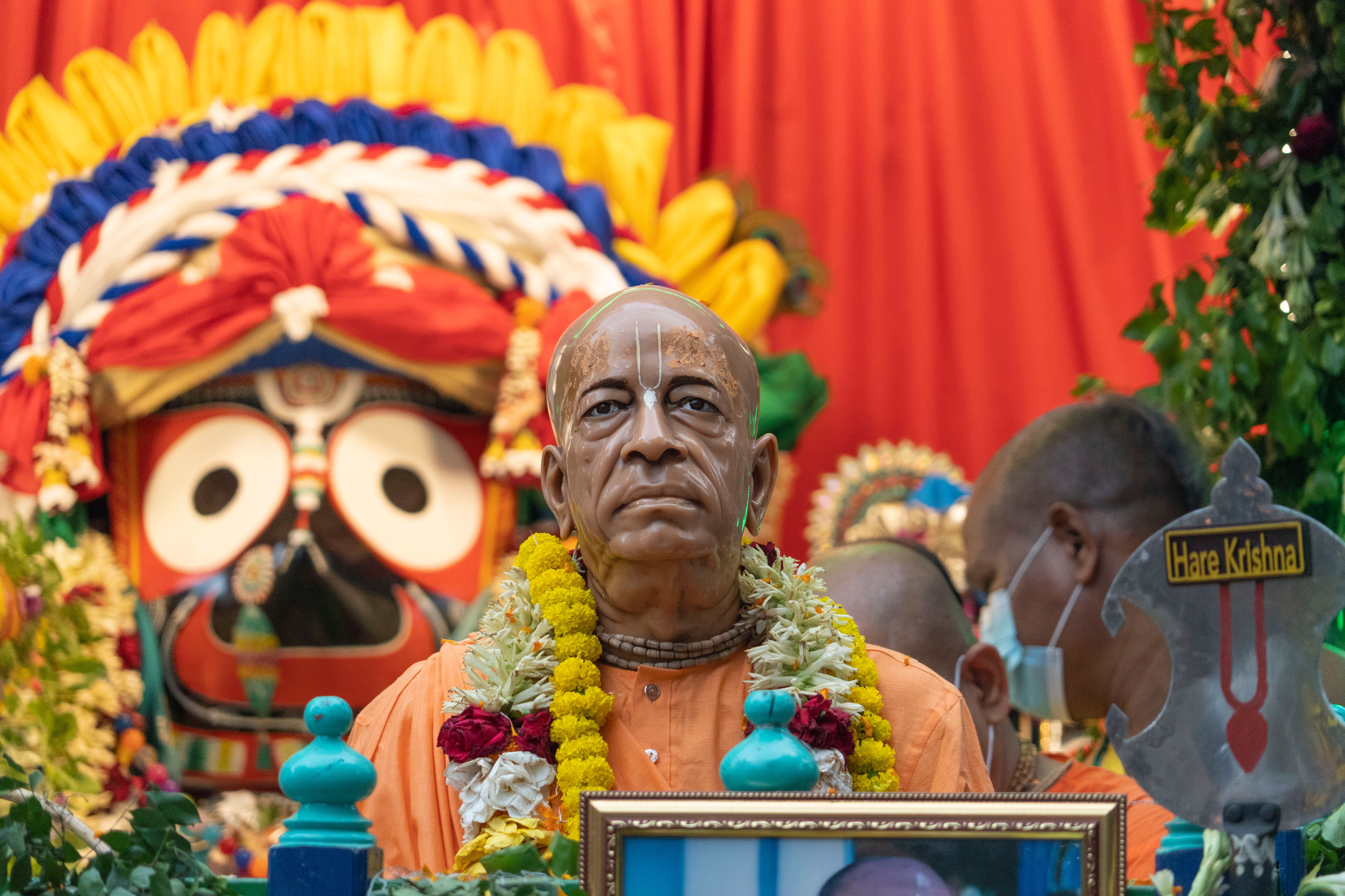 Colorful Hindu festival with Jagannath deity and a spiritual leader's statue.