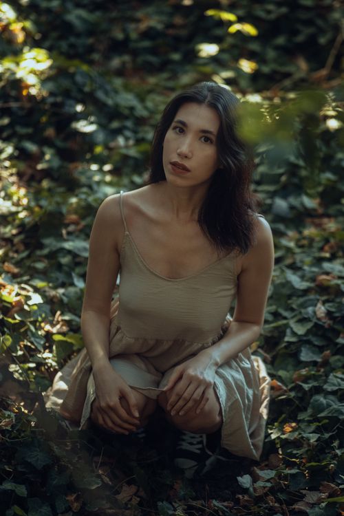 Free Brunette woman crouching in forest, wearing stylish summer dress, showcasing modern fashion. Stock Photo