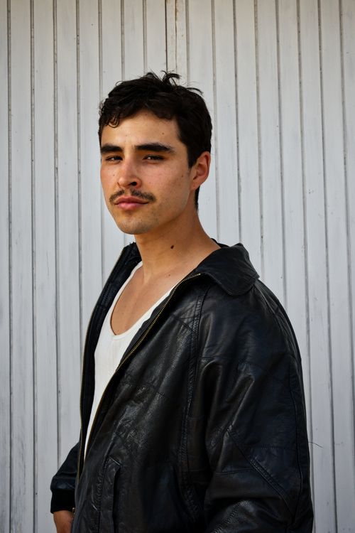 Free A fashionable man poses confidently in a leather jacket against a white panel background. Stock Photo