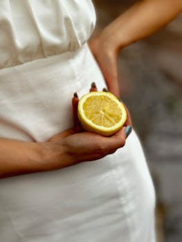 A woman in a white dress holding a sliced lemon, highlighting freshness and summertime.